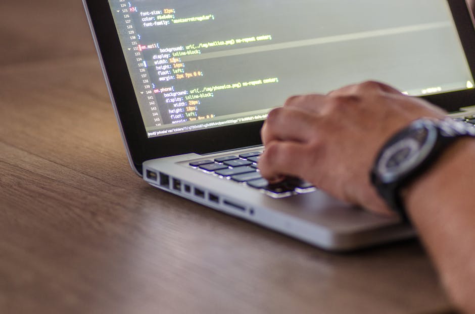 A close-up view of a laptop screen displaying lines of programming code, with a dark background illuminated by a soft blue and pink glow, suggesting a dimly lit environment. The code includes syntax h